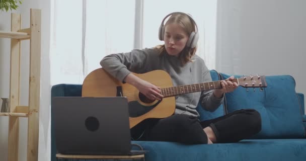 Teini-ikäinen oppii kaksi sointua kitarassa. Nainen kuulokkeiden kanssa poimii musikaalisen sävelen.. - Materiaali, video