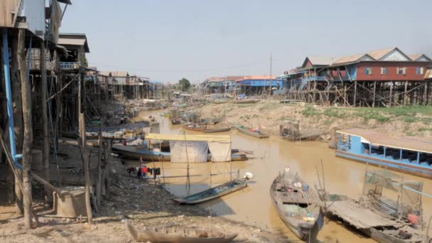 zijaanzicht van een lange staart vissersboot varen door een drijvend dorp in de rivier tijdens het droge seizoen - Video