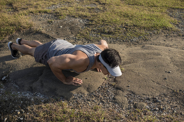 Un ajuste asiático chicos hace flexiones en un estéril roca superficie después de un sendero correr o caminar en el campo. - Foto, Imagen