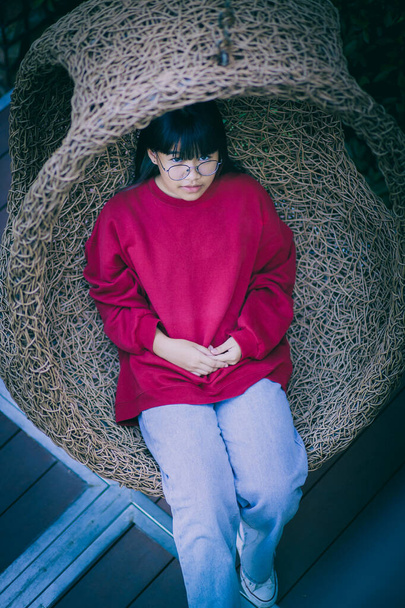 azjatycki nastolatek siedzi w bambus huśtawka w domu taras  - Zdjęcie, obraz