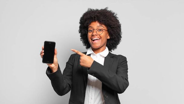 young afro businesswoman looking excited and surprised pointing to the side and upwards to copy space. business concept - Fotó, kép