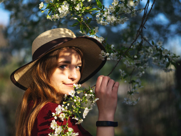 Moda wiosenny portret kobiety w kwitnącym ogrodzie. Szczęśliwa kobieta w kapeluszu - Zdjęcie, obraz
