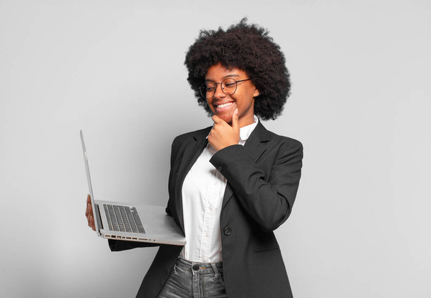 νεαρή Αφρο επιχειρηματίας χαμογελά με μια ευτυχισμένη, σίγουρη έκφραση με το χέρι στο πηγούνι, αναρωτιούνται και κοιτάζοντας προς τα πλάγια. επιχειρηματική ιδέα - Φωτογραφία, εικόνα