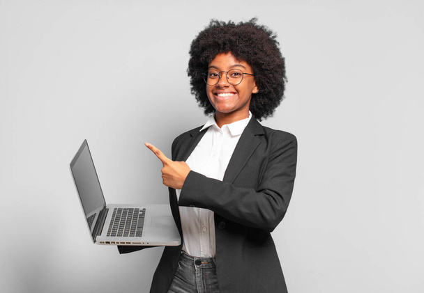 young afro businesswoman smiling cheerfully, feeling happy and pointing to the side and upwards, showing object in copy space. business concept - Foto, Imagen