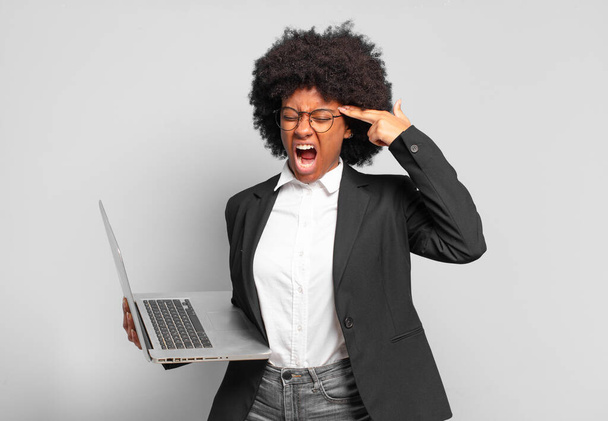 young afro businesswoman looking unhappy and stressed, suicide gesture making gun sign with hand, pointing to head. business concept - Foto, Imagen