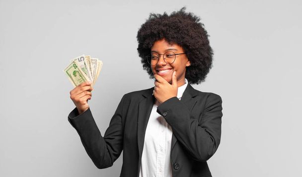 giovane donna d'affari afro sorridente con una felice, espressione fiduciosa con mano sul mento, chiedendo e guardando di lato. concetto di business - Foto, immagini