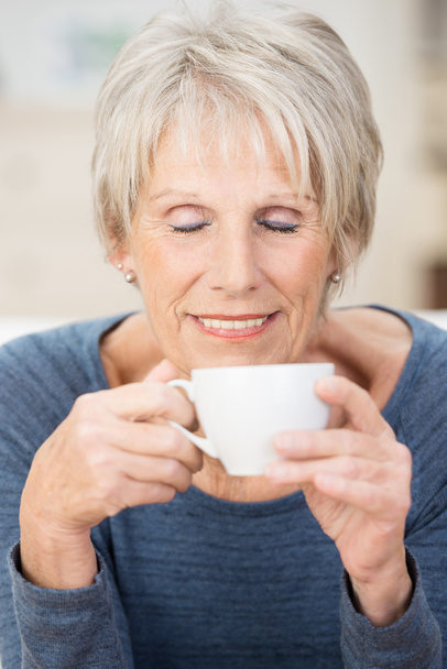 Attractive senior woman savoring a cup of coffee - Photo, Image