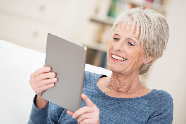 Elderly woman smiling as she reads her tablet - 写真・画像