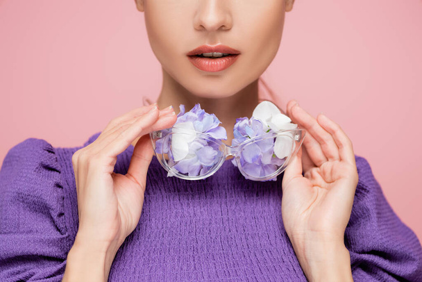 částečný pohled na ženu v purpurové blůze držící brýle s květy izolované na růžové - Fotografie, Obrázek