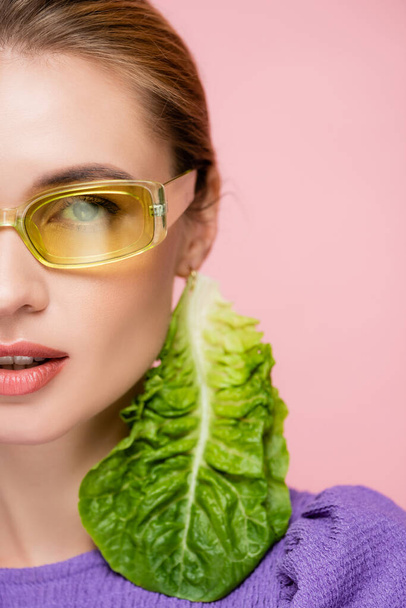 close up view of young woman in colored eyeglasses, with fresh lettuce earring isolated on pink - Foto, afbeelding