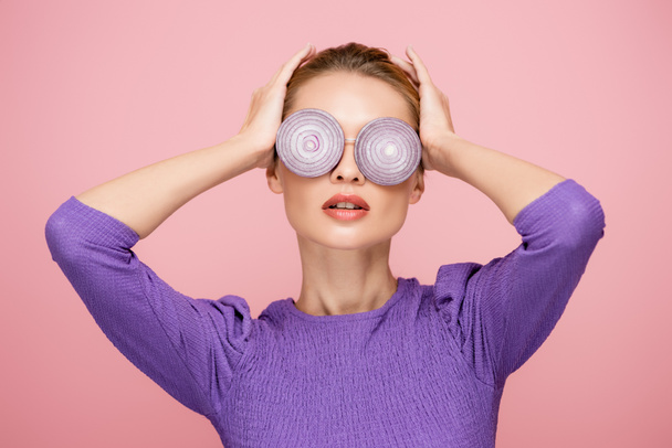 young woman touching head while posing in eyeglasses with onion rings isolated on pink, surrealism concept - Photo, Image