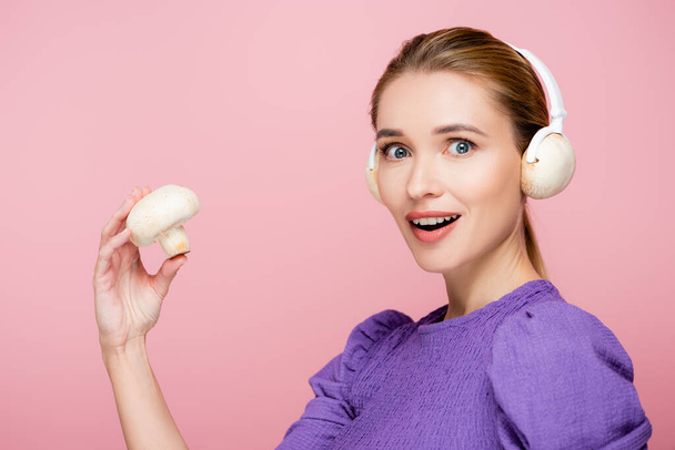ενθουσιασμένοι γυναίκα με μανιτάρια σε ακουστικά κρατώντας champignon απομονώνονται σε ροζ - Φωτογραφία, εικόνα