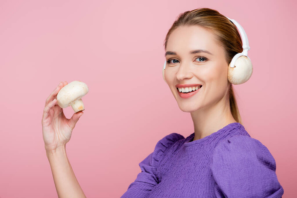 mladá žena s houbami ve sluchátkách s úsměvem na kameru izolované na růžové - Fotografie, Obrázek