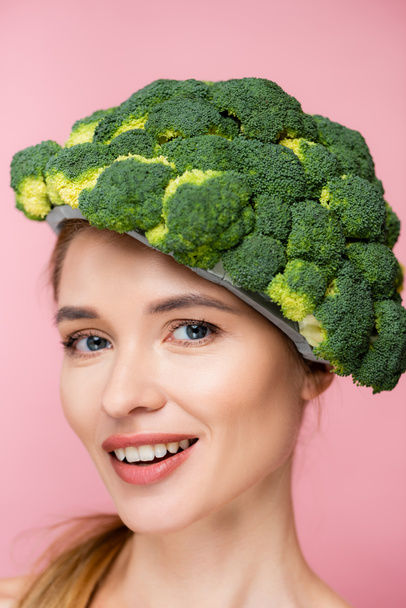portrait of cheerful woman in hat made of fresh broccoli isolated on pink, surrealism concept - Photo, Image