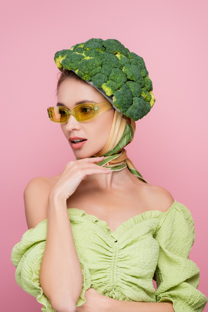 sensual woman in colored eyeglasses and hat made of fresh broccoli isolated on pink, surrealism concept - Photo, Image