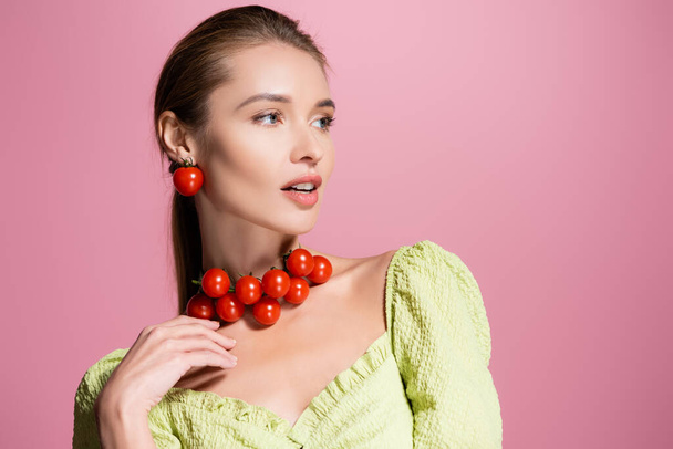sensual woman in red cherry tomatoes necklace looking away isolated on pink - Photo, Image