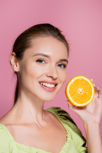 Charmante Frau mit natürlichem Make-up hält die Hälfte der reifen Orange isoliert auf rosa - Foto, Bild