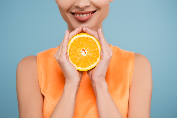 oříznutý pohled na usmívající se ženu s polovinou zralé oranžové izolované na modré - Fotografie, Obrázek
