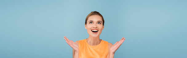 excited woman in orange singlet looking up isolated on blue, banner - Photo, Image