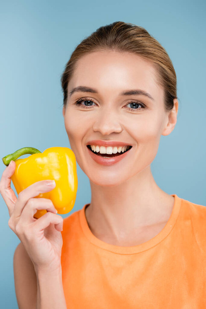 χαρούμενη νεαρή γυναίκα με φυσικό μακιγιάζ ποζάρουν με πιπεριά απομονωμένη στο μπλε - Φωτογραφία, εικόνα