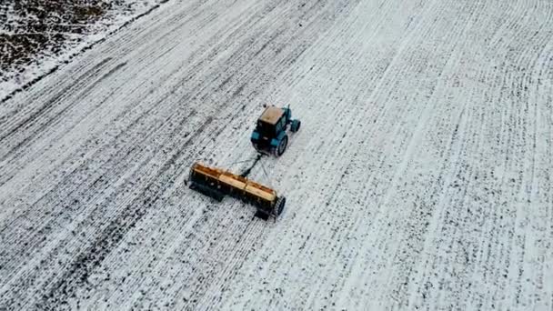 Vue aérienne des machines agricoles fertilisant le sol avec de l'insecticide dans un champ blanc avec de la neige en utilisant un tracteur en hiver - Séquence, vidéo