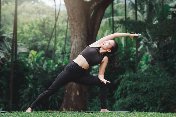 Donna asiatica che pratica yoga si estende lateralmente per iniziare a preparare le pose di preparazione per la gru laterale Pose per Parsva Bakasana sul tappeto nel parco all'aperto. - Foto, immagini
