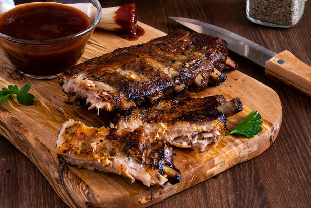 Close-up van spareribs op een houten plank met barbecue saus achter. - Foto, afbeelding