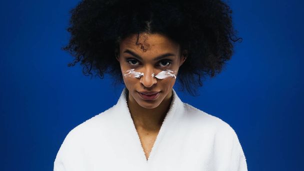 Afroamerikanerin mit Gesichtscreme isoliert auf blau  - Foto, Bild