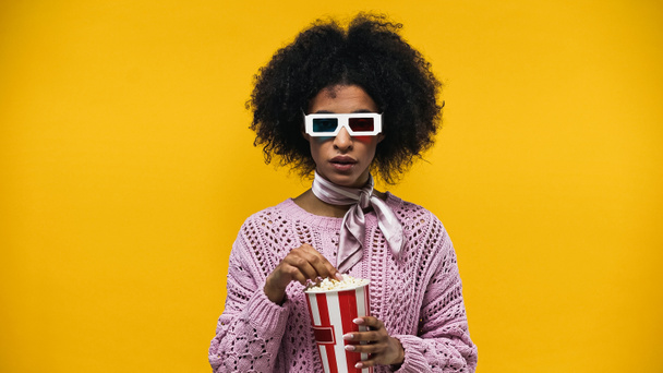 Африканская американка в 3D очках держит попкорн изолирован на желтый - Фото, изображение