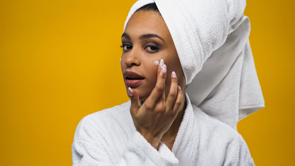 Mujer afroamericana aplicando crema facial aislada en amarillo  - Foto, Imagen