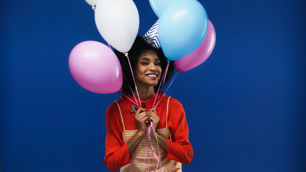 Sorridente donna afroamericana che tiene i palloncini isolati sul blu - Foto, immagini