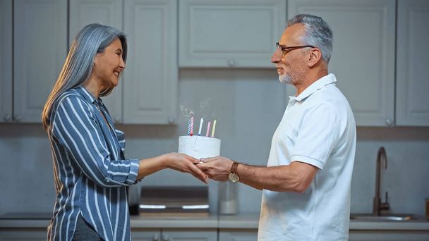 side view of happy senior asian woman taking birthday cake from smiling husband - Photo, image