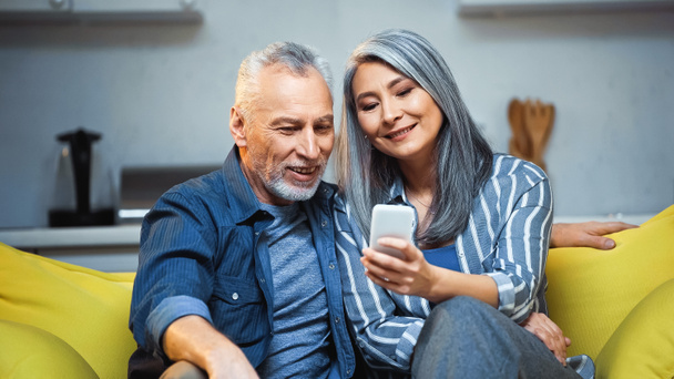 smiling asian grey haired woman using smartphone near happy husband - Zdjęcie, obraz
