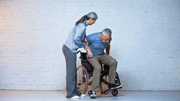 elderly asian woman helping handicapped husband to sit in wheelchair - Foto, Imagem