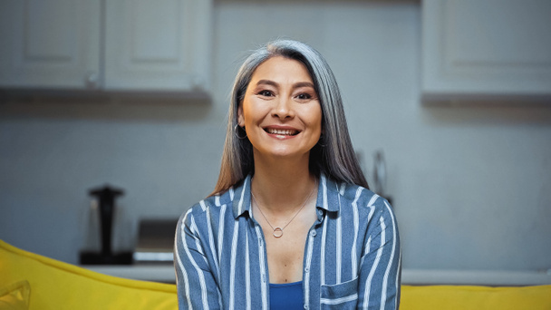 happy senior asian woman in striped shirt smiling at camera at home - Фото, зображення