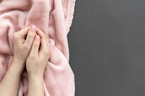 Las manos femeninas con la manicura hermosa - las uñas rosadas desnudas sobre la tela pálida rosada esponjosa y el fondo gris de papel con el espacio de copia - Foto, Imagen
