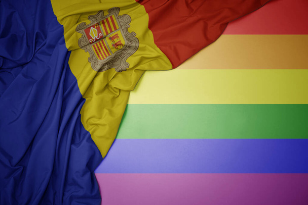 schwenken bunte Nationalflagge von andorra auf einem homosexuellen Regenbogenfahne Hintergrund. - Foto, Bild