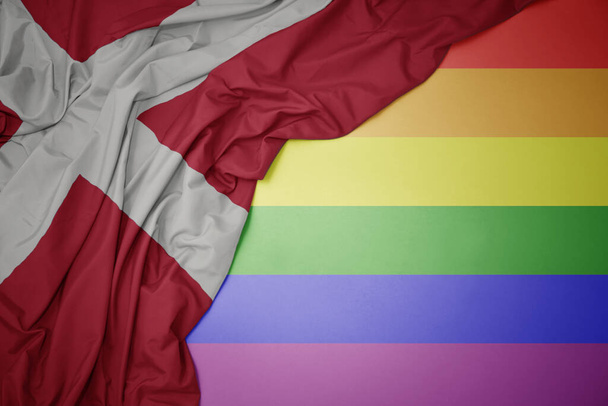 размахивая красочным национальным флагом денмарка на фоне радужного флага геев. - Фото, изображение