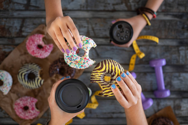 Donuts y mancuerna en manos de dos mujeres. Concepto de comida chatarra. - Foto, imagen