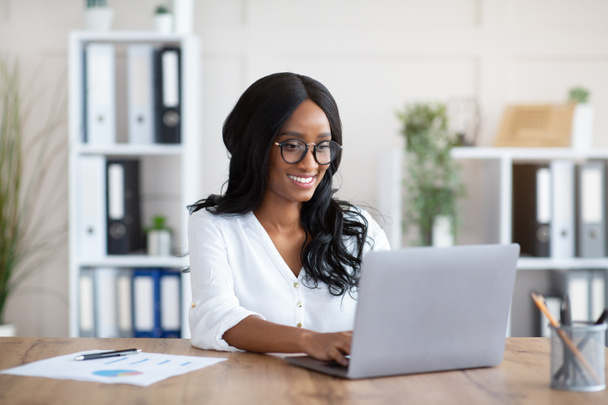 Όμορφη μαύρη επιχειρηματίας που εργάζεται με φορητό υπολογιστή στο γραφείο στο γραφείο - Φωτογραφία, εικόνα