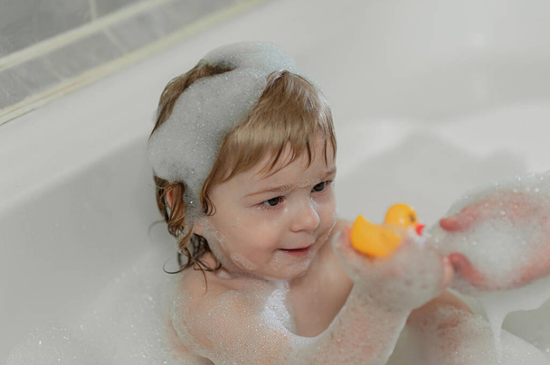 bébé dans le bain moussant jouant avec le canard en caoutchouc jaune. Photo de haute qualité - Photo, image