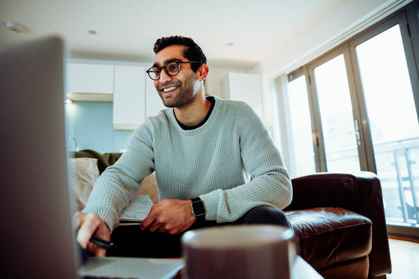 Sorrindo homem de negócios de raça mista digitando no laptop sentado no sofá trabalhando em casa - Foto, Imagem