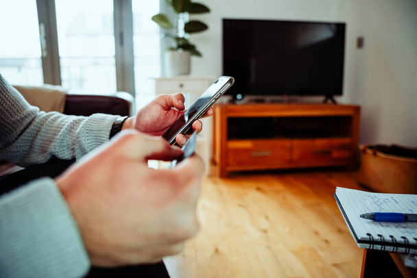 Közelkép vegyes verseny üzletember ül a kanapén gépelés okostelefonon a nappaliban - Fotó, kép