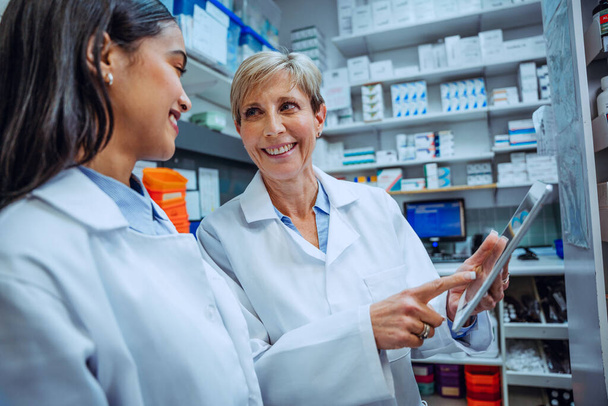 Iäkäs farmaseutti opettaa uutta harjoittelijaa työskentelemään digitaalinen tabletti seisoo lääkehuoneessa apteekissa  - Valokuva, kuva