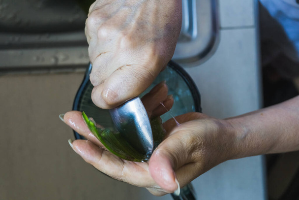 Mujer adulta irreconocible vertiendo gel de aloe en un frasco de licuadora con una cuchara en una cocina - Foto, imagen