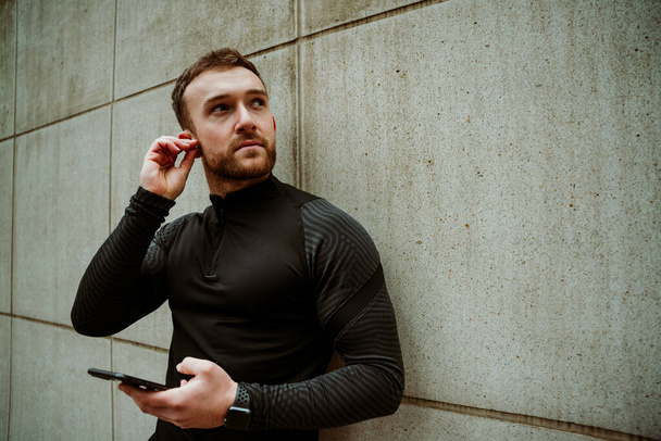 athlète masculin caucasien changer la musique sur smartphone écoute avec écouteurs tout en cours d'exécution en plein air - Photo, image