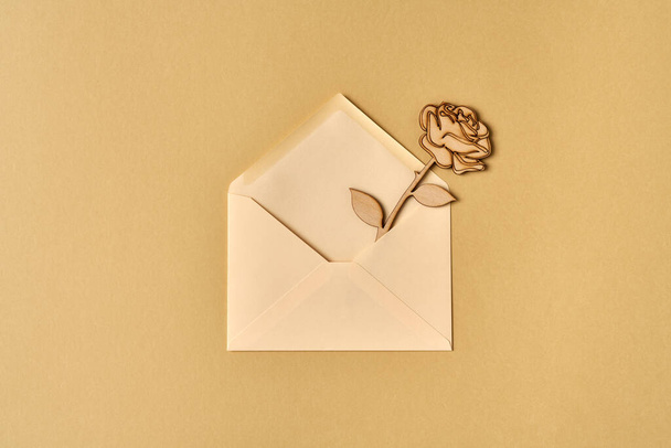 Wooden rose in an envelope on beige paper background, top view - Photo, Image