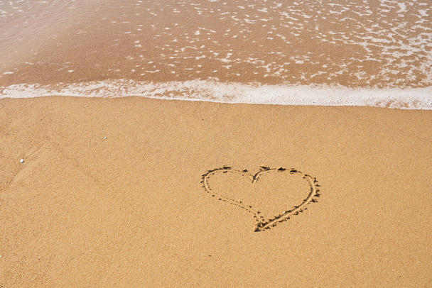 Καρδιά ζωγραφισμένη στην άμμο στην παραλία και αφρός από τα κύματα. Ημέρα του Αγίου Βαλεντίνου έννοια. - Φωτογραφία, εικόνα