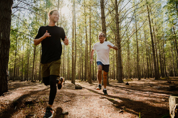 Caucasian father and teen son brothers exercising in lush forest running in the woodlands - Photo, Image