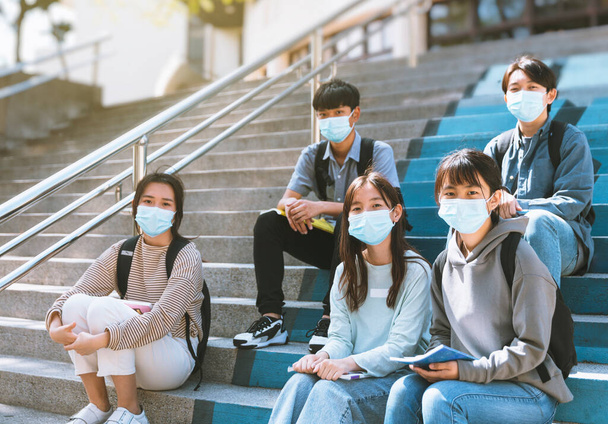 молоді студенти носять маски для обличчя і сидять на сходах
 - Фото, зображення